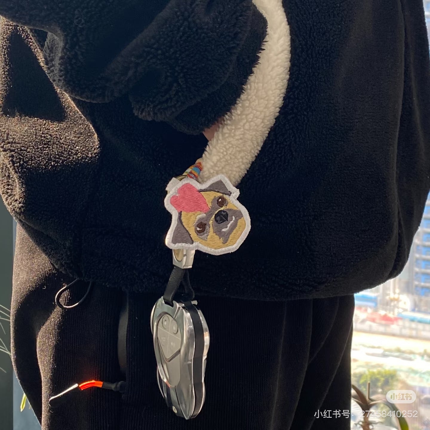 Black fleece jacket with a cartoon dog keychain on a blurred outdoor background