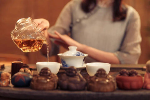 In front of the tea table is a row of tea pets, and behind them stands a Chinese lady in a traditional cheongsam, pouring tea over the tea pets.