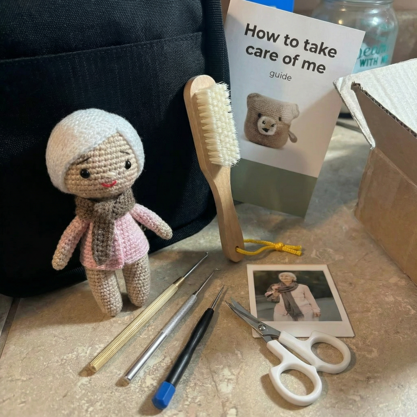 Small crocheted doll, brush, tools, and a 'How to take care of me' guide on a surface.