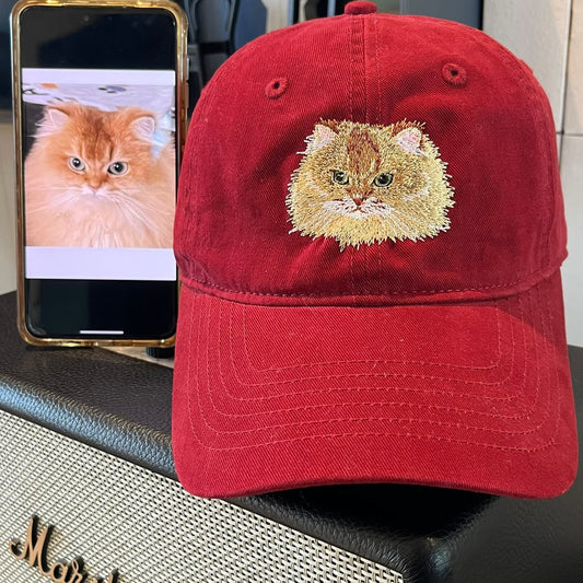 Red cap with cat embroidery next to a phone displaying a cat image, on a Marshall amplifier.